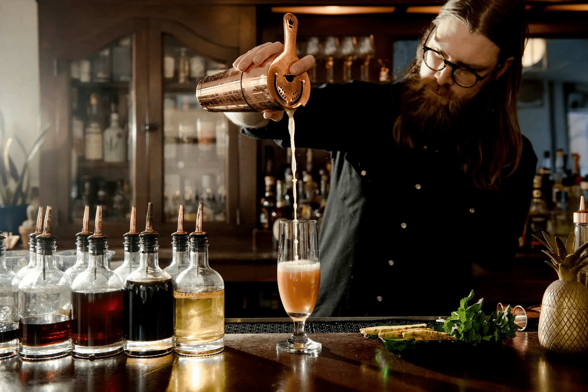 A photo of Bartender Brendan Biggins pouring a cocktail into a glass